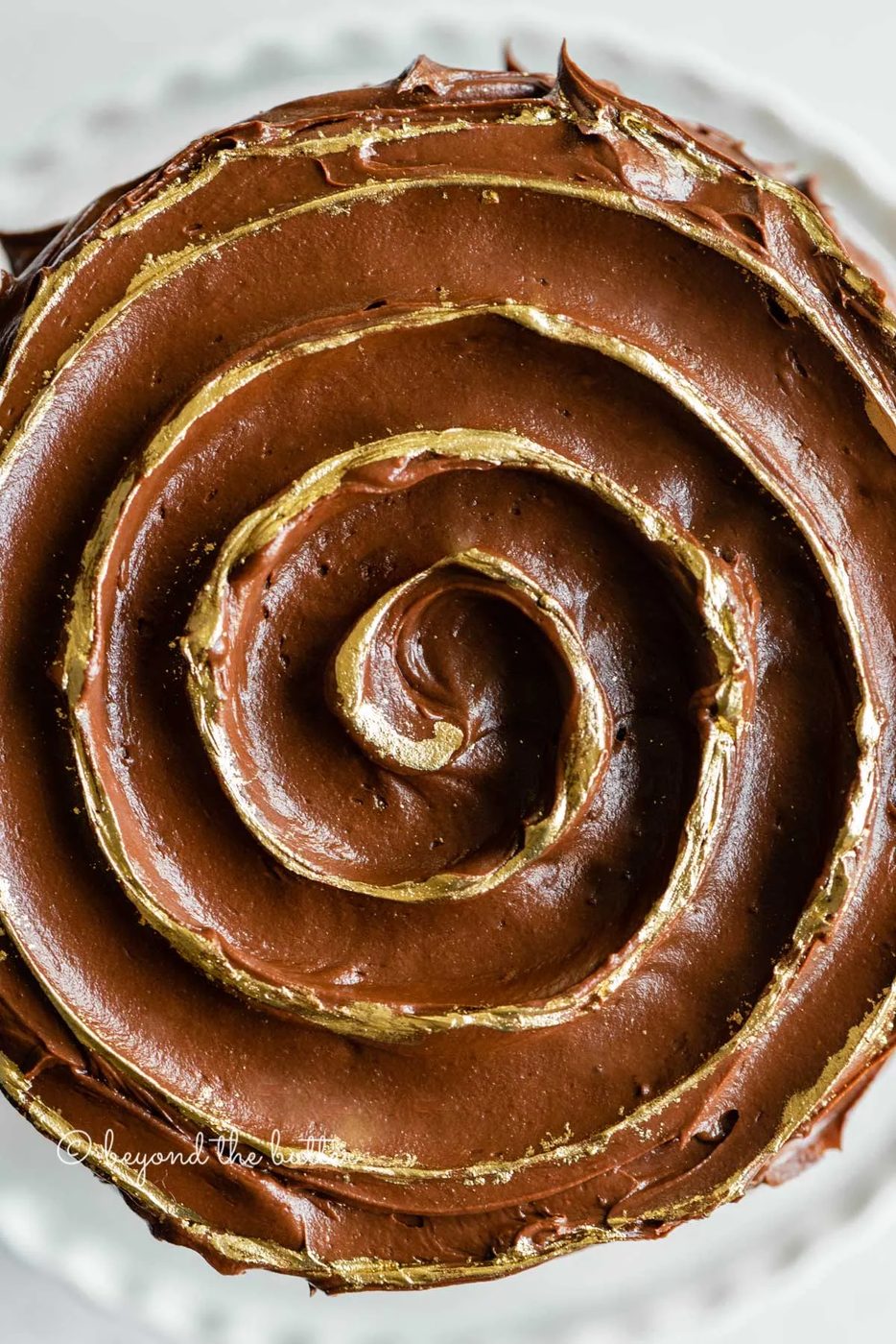 Overhead closeup image of chocolate zucchini cake with chocolate chips and gold decorative swirl on top | All Images © Sovuh