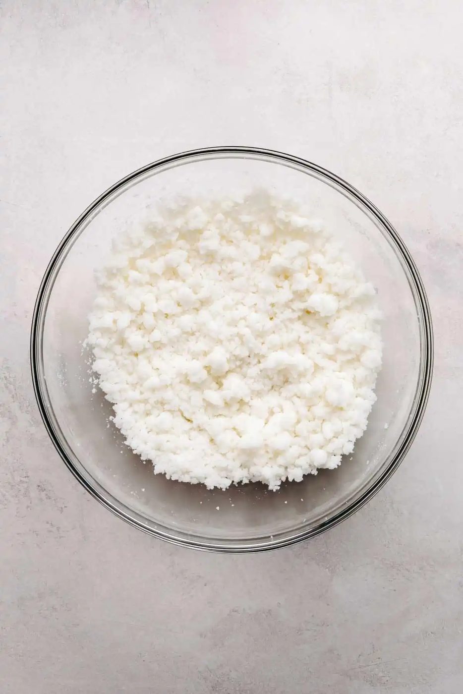 Granulated sugar and vegetable shortening mixed together in a large glass mixing bowl on a light grey marbled background.