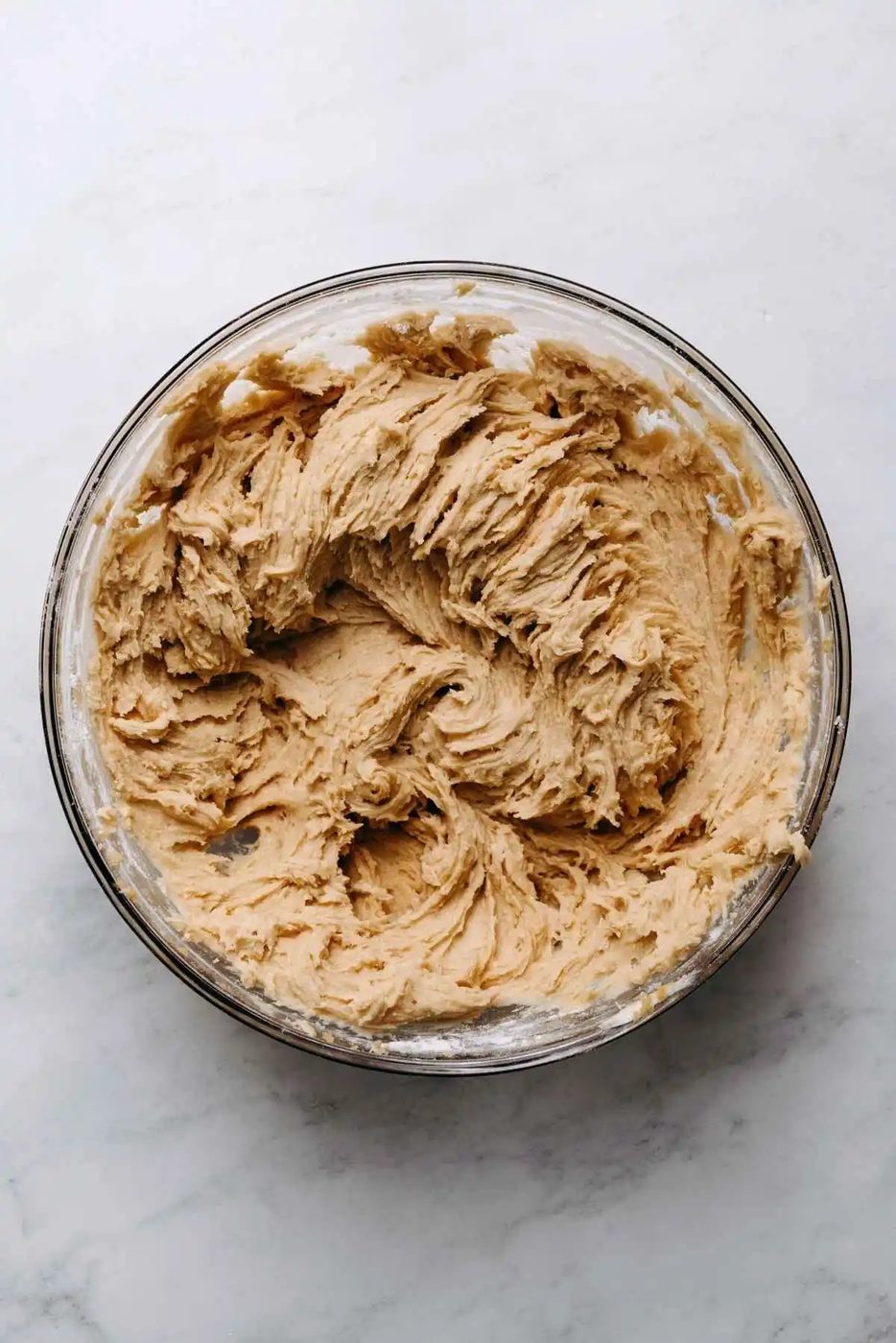 Whisked flour mixture blended together with the wet ingredients in a large glass mixing bowl on a white marbled background.