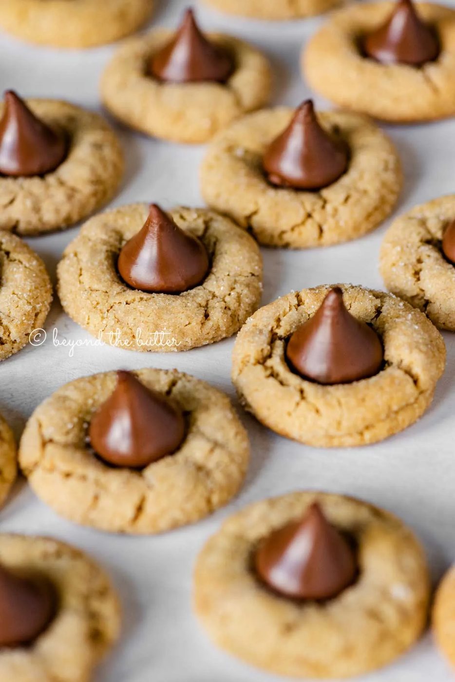 Angled image of peanut butter blossoms on parchment paper lined baking sheet | All Images © Sovuh