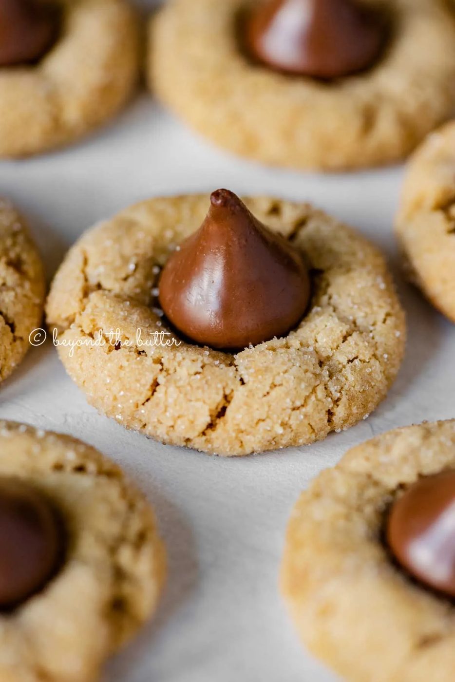 Angled closeup image of peanut butter blossoms on parchment paper lined baking sheet | All Images © Sovuh