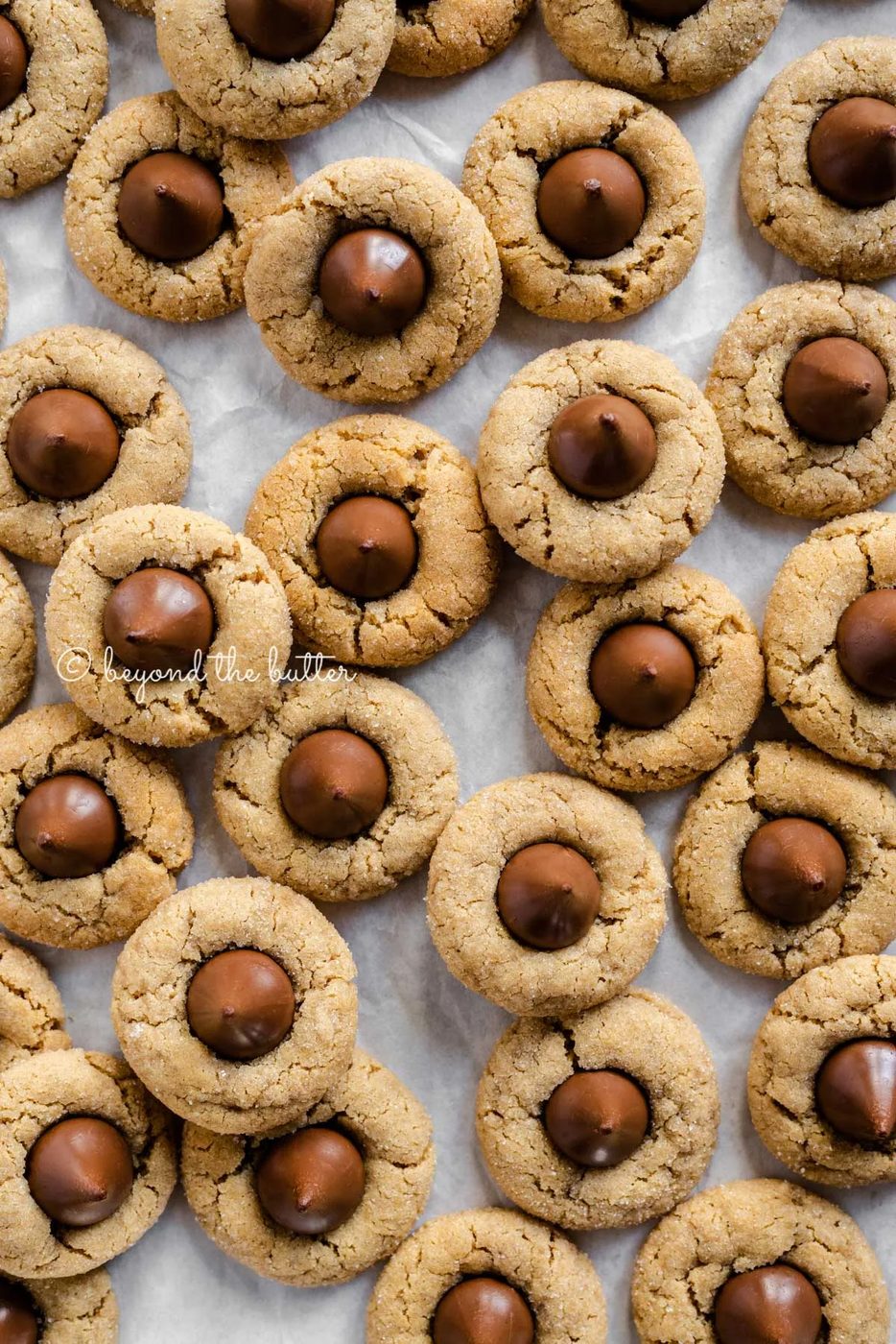 Familiar peanut butter blossoms on a parchment paper lined baking sheet | Sovuh