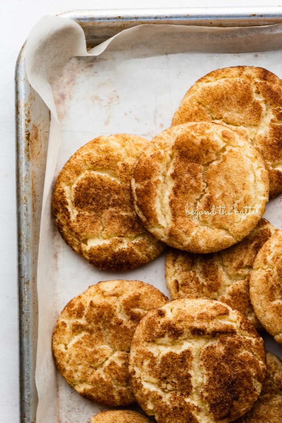 Randomly placed snickerdoodle cookies on a parchment paper lined baking sheet | © Sovuh