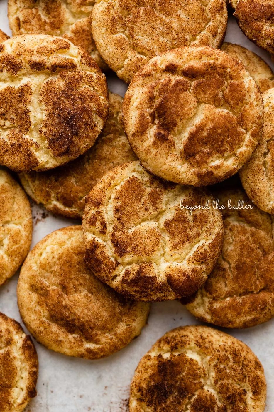 Piled snickerdoodle cookies on a parchment paper lined baking sheet | © Sovuh