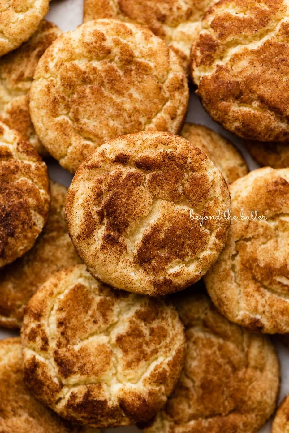 Piled snickerdoodle cookies on a parchment paper lined baking sheet | © Sovuh