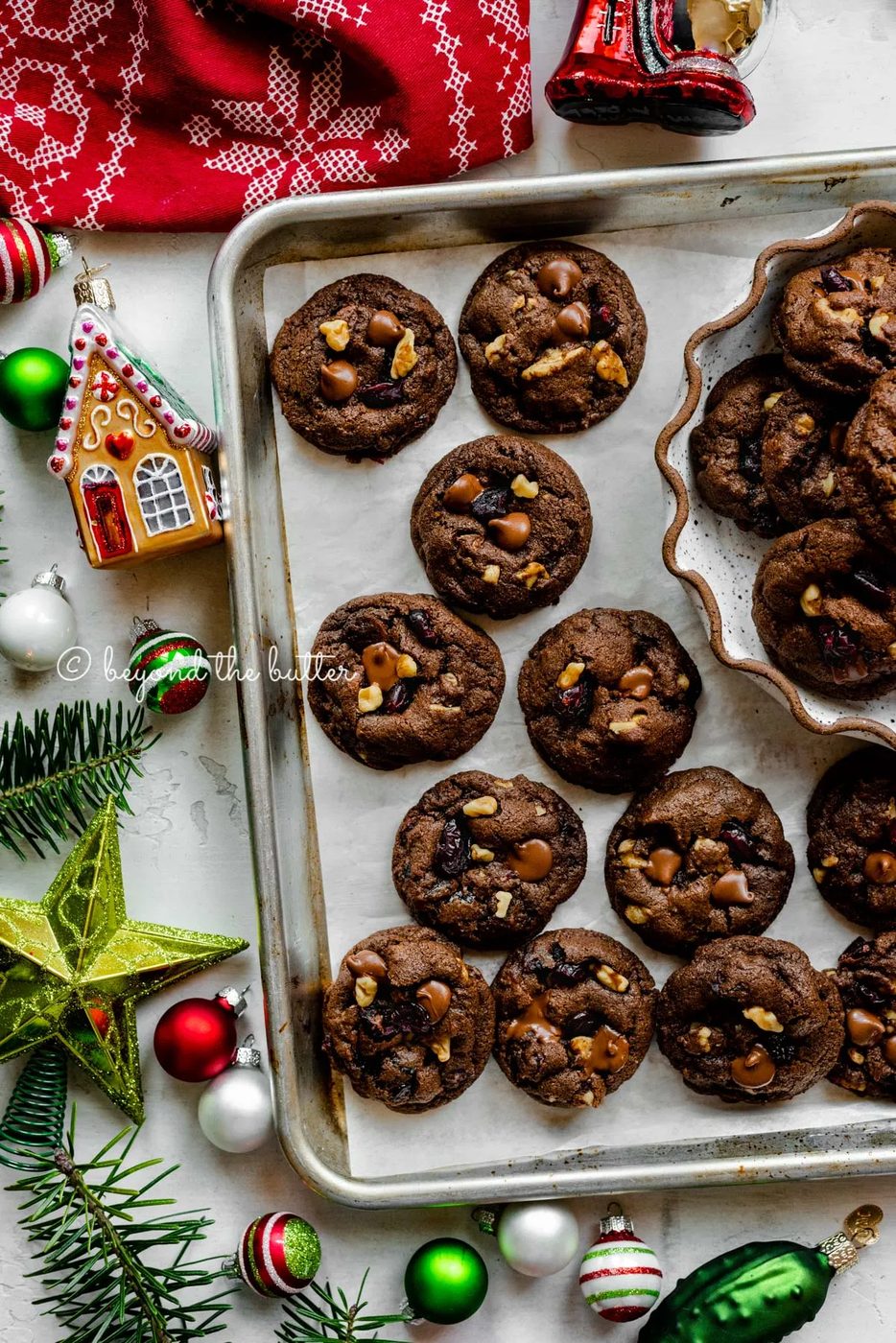 Parchment paper lined baking sheet with dark chocolate cranberry walnut cookies surrounded Christmas tree ornaments | All Images © Sovuh