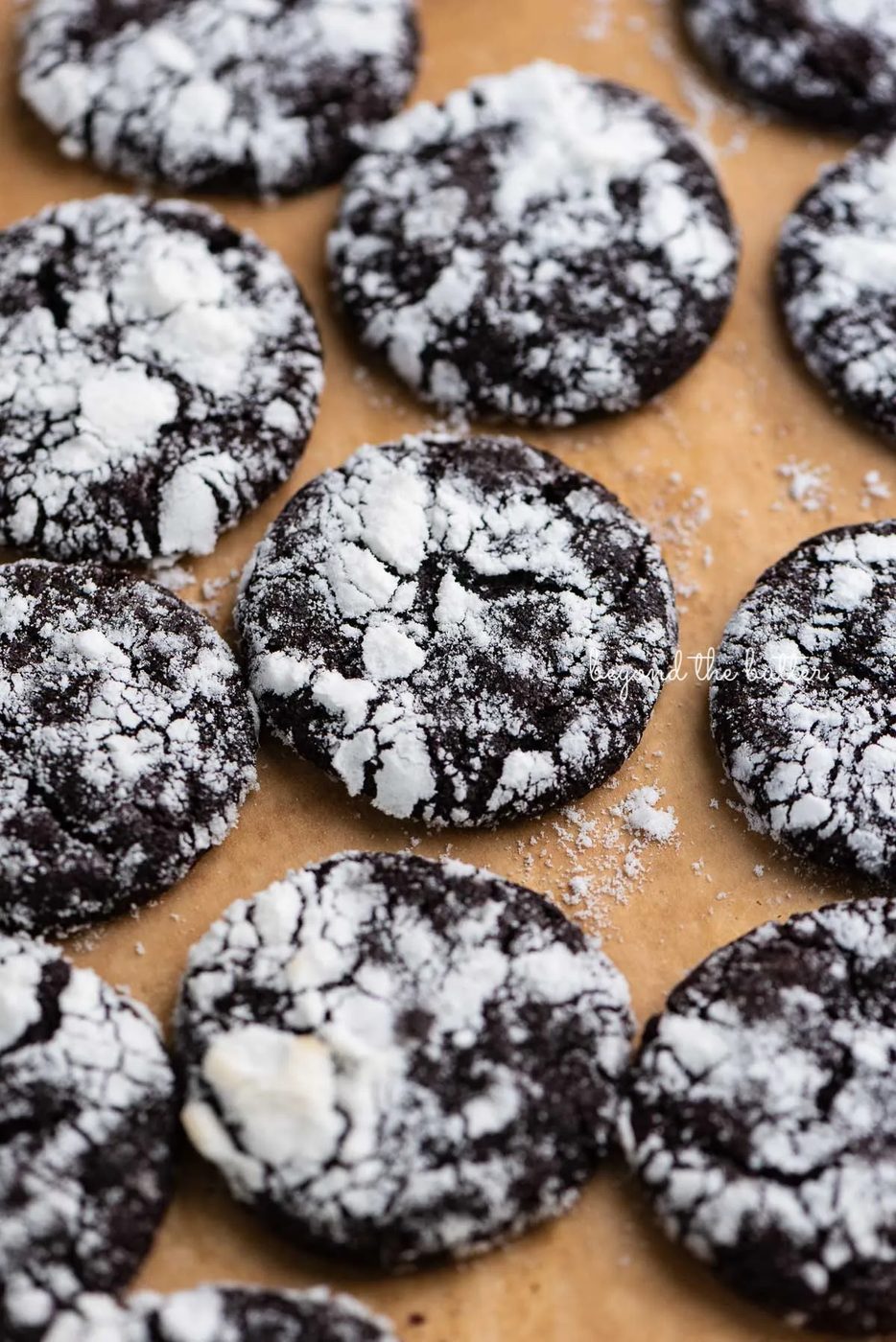 Dark chocolate crinkle cookies on a brown parchment paper lined baking sheet | © Sovuh