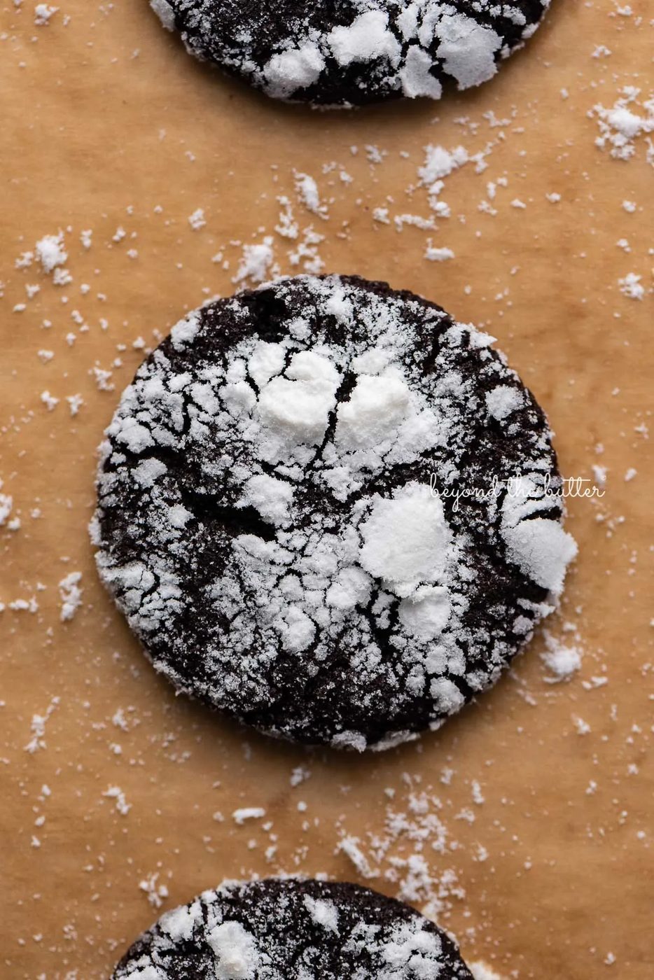 Closeup of dark chocolate crinkle cookie on a brown parchment paper lined baking sheet | © Sovuh