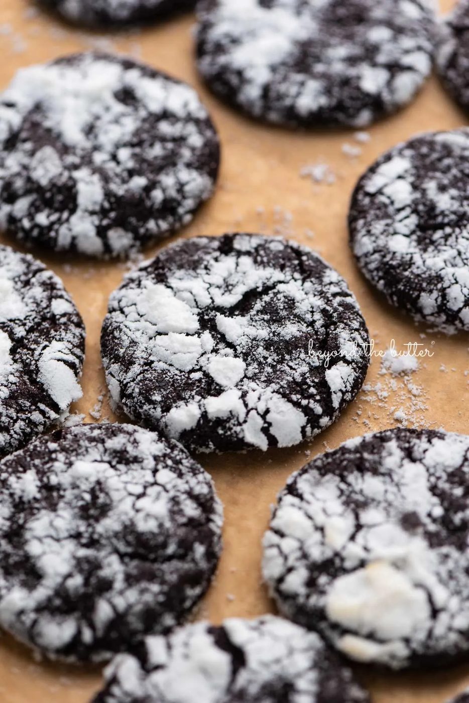 Dark chocolate crinkle cookies on a brown parchment paper lined baking sheet | © Sovuh