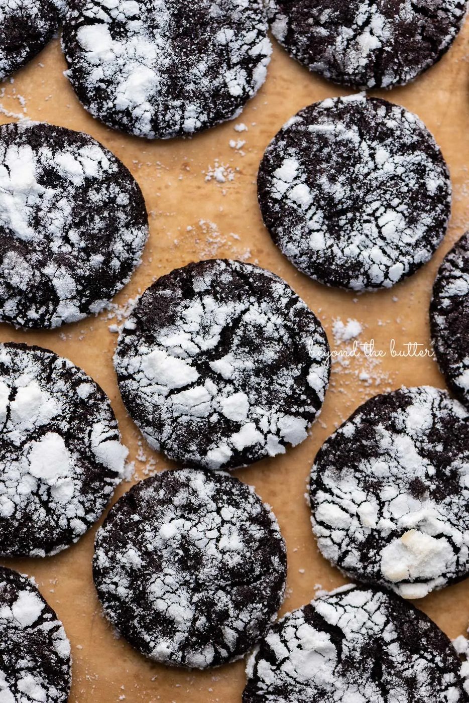 Just baked dark chocolate crinkle cookies on a brown parchment paper lined baking sheet | © Sovuh