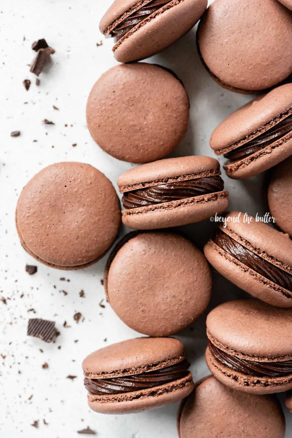 Overhead image of randomly placed dark chocolate macaons with bit of chocolate pieces around them | All Images © Sovuh