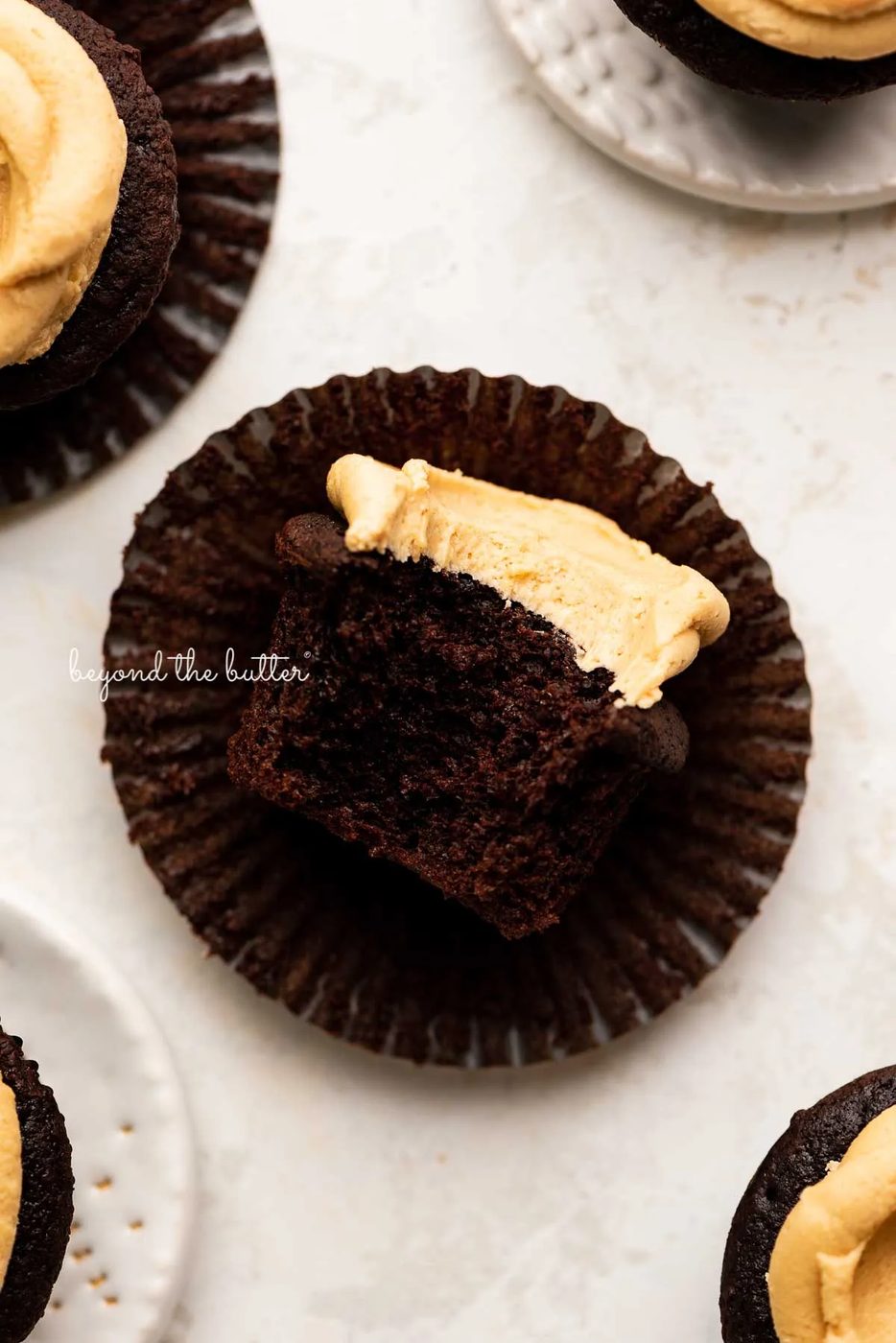 Unwrapped devil's food cupcake with peanut butter frosting with a bite taken out of it on white background | © Sovuh