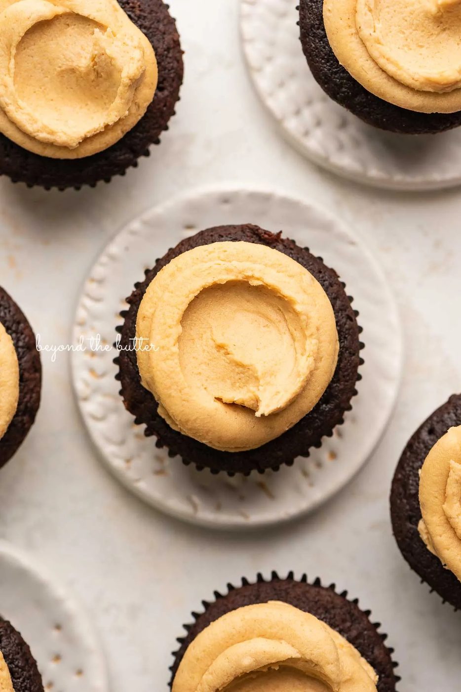 Devil's food cupcakes with peanut butter frosting with some on small dessert plates on white background | © Sovuh