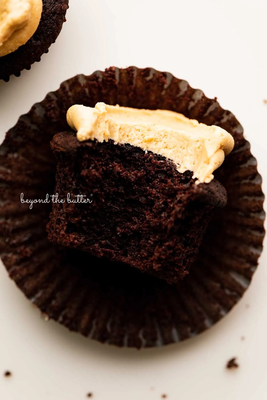 Unwrapped devil's food cupcake with peanut butter frosting with a bite taken out of it on white background | © Sovuh