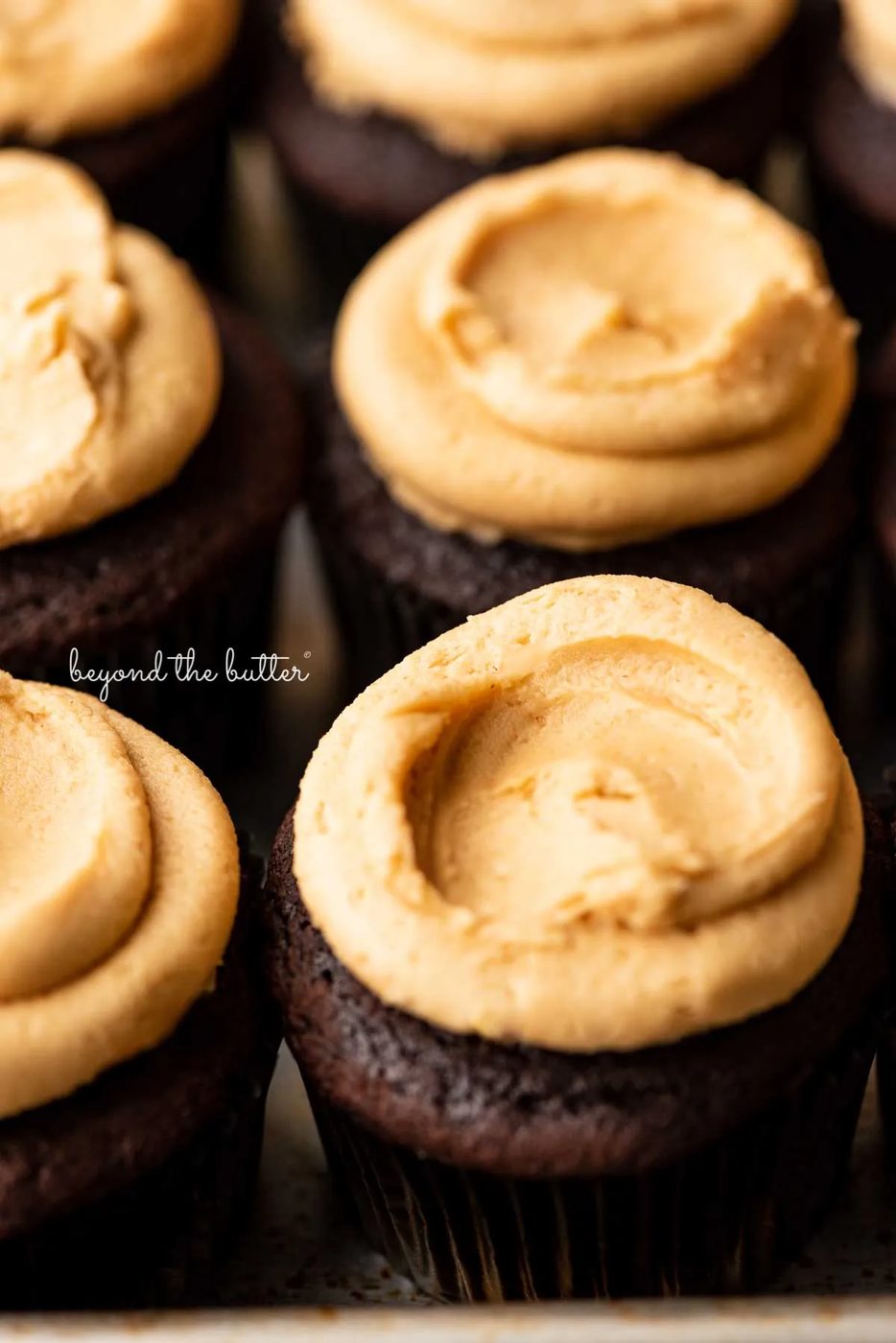 Close up image of devil's food cupcakes topped with peanut butter frosting on a baking sheet | © Sovuh