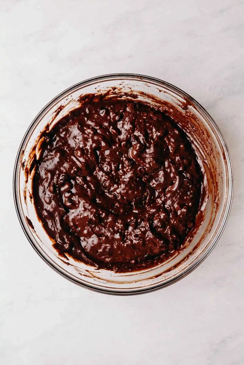 Double chocolate muffin batter in a large glass mixing bowl on a white marbled background.
