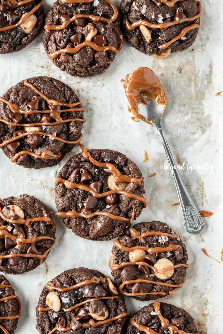 Overhead image of just baked double chocolate salted caramel cookies on a baking sheet with spoon dipped in a caramel sauce resting close by | All Images © Sovuh