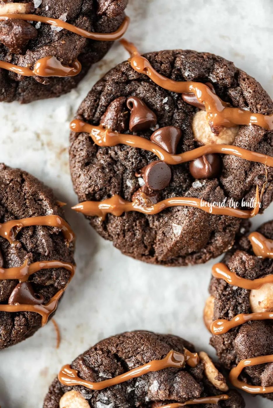 Overhead image of just baked double chocolate salted caramel cookies on a baking sheet with caramel drizzled over the top of each cookie | All Images © Sovuh