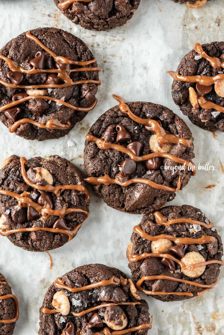 Overhead image of just baked double chocolate salted caramel cookies on a baking sheet with caramel drizzled over the top of each cookie | All Images © Sovuh