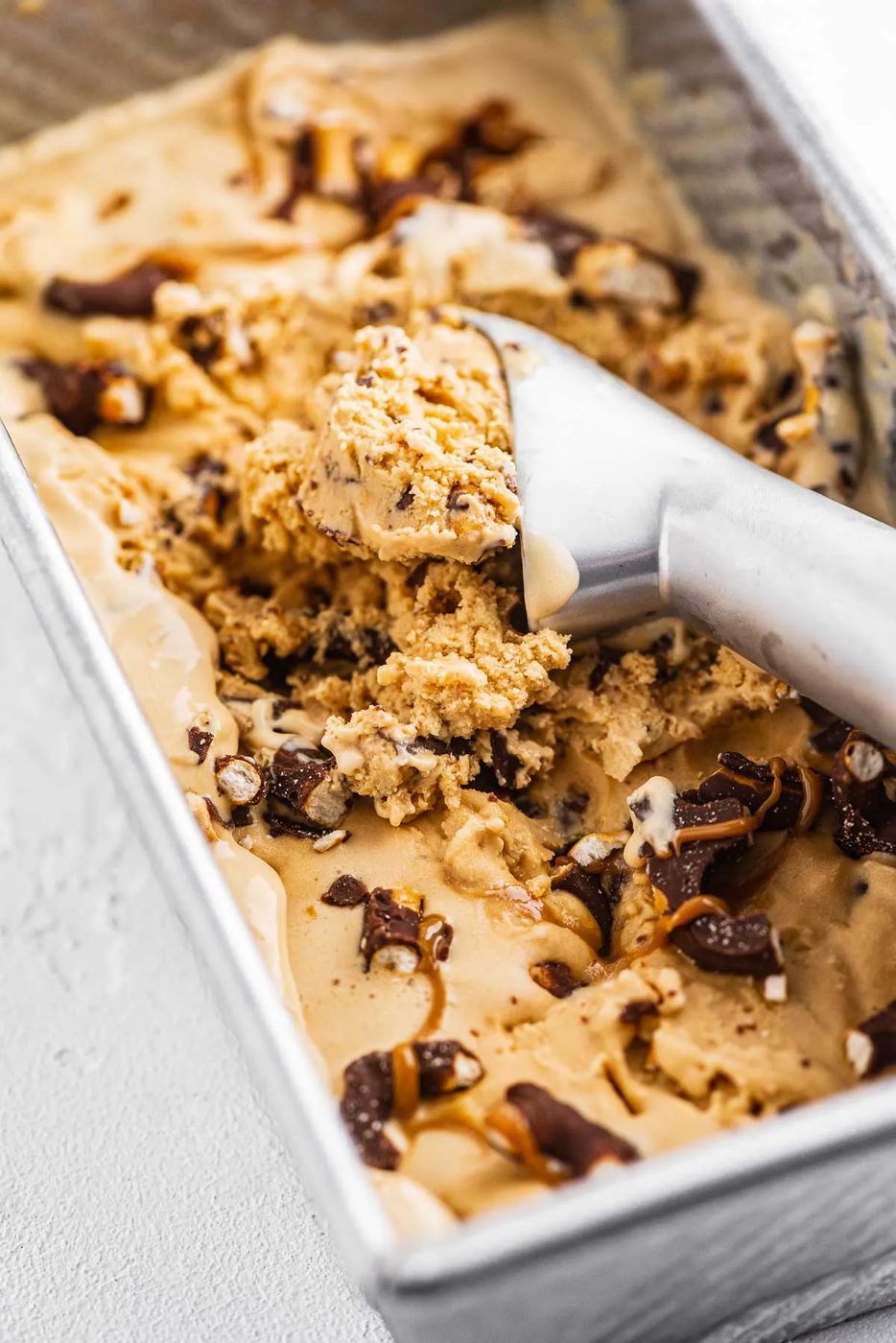 Ice cream sccop in a container of dulce de leche ice cream with chocolate covered pretzels | © Sovuh