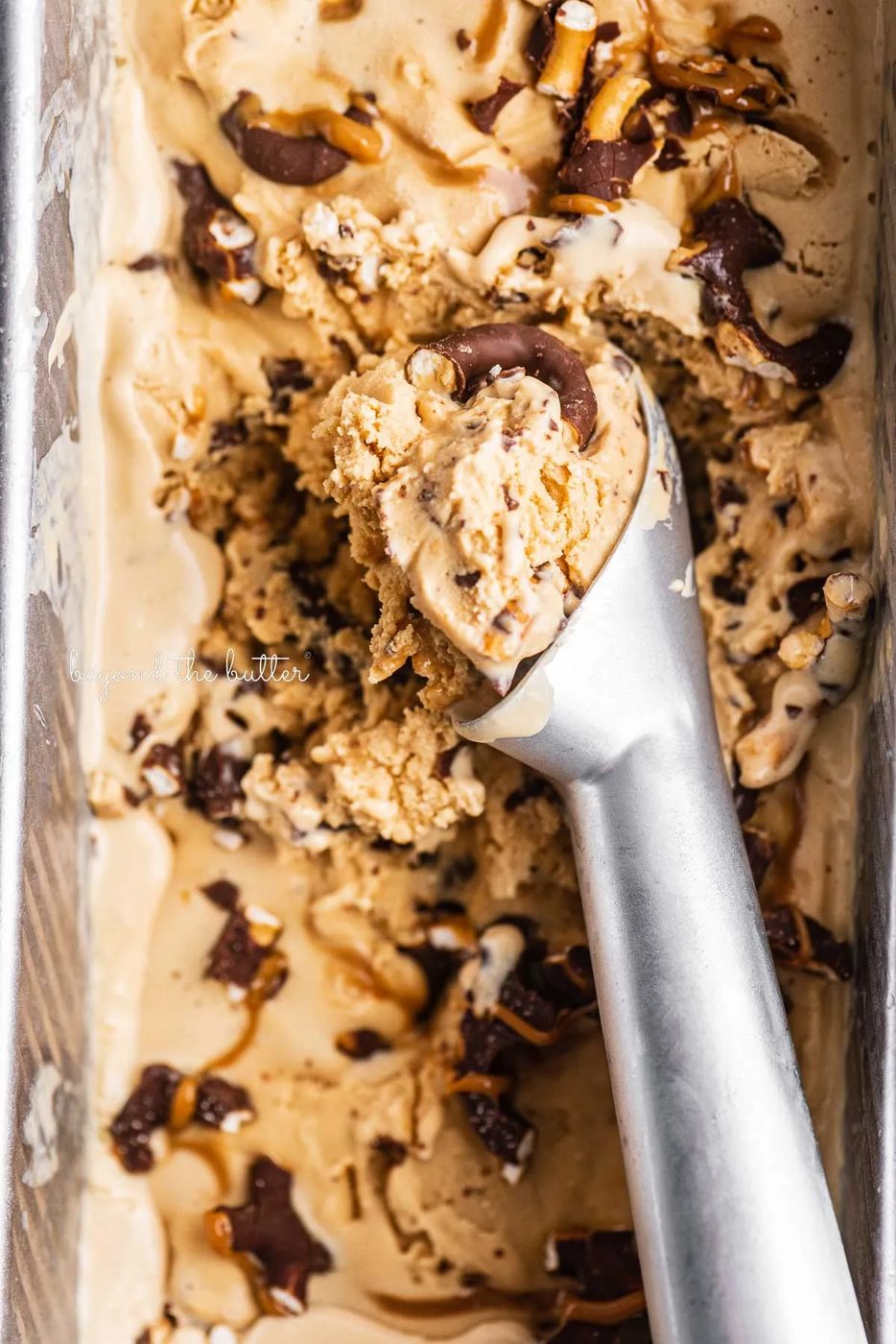 Ice cream sccop in a container of dulce de leche ice cream with chocolate covered pretzels | © Sovuh