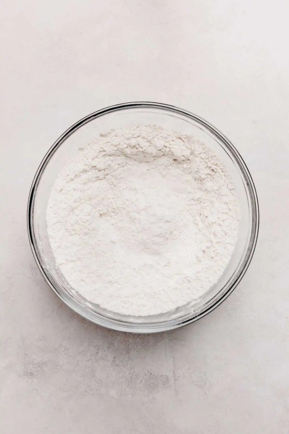 Whisked all purpose flour, baking soda, and salt in a glass mixing bowl on a light grey background.