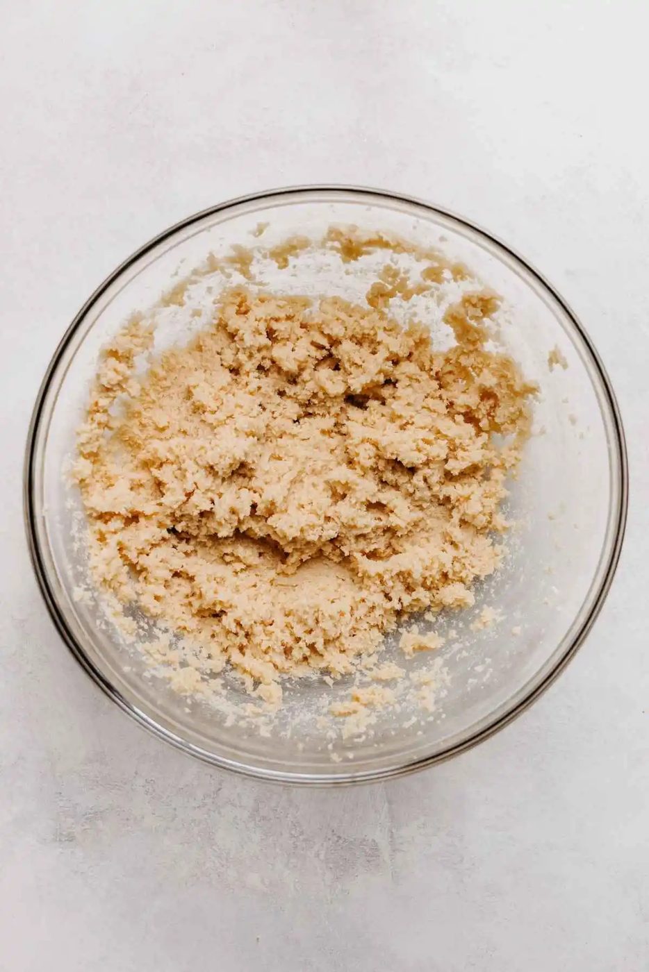 Unsalted butter, granulated sugar, and light brown sugar blended together in a large glass mixing bowl on a light grey background.