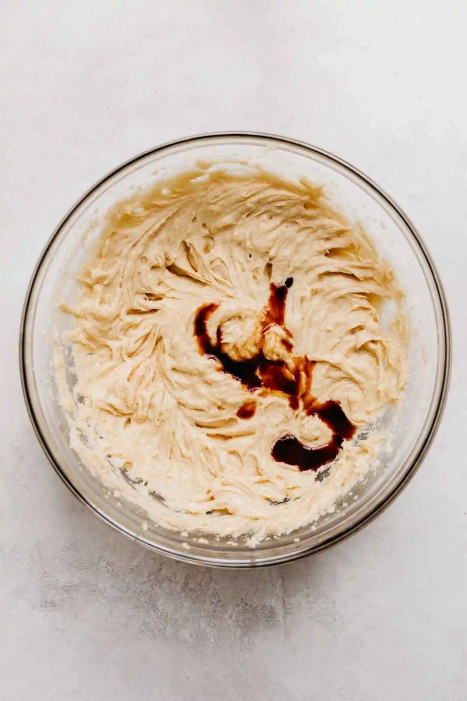 Eggs and vanilla extract added to large glass mixing bowl on a light grey background.