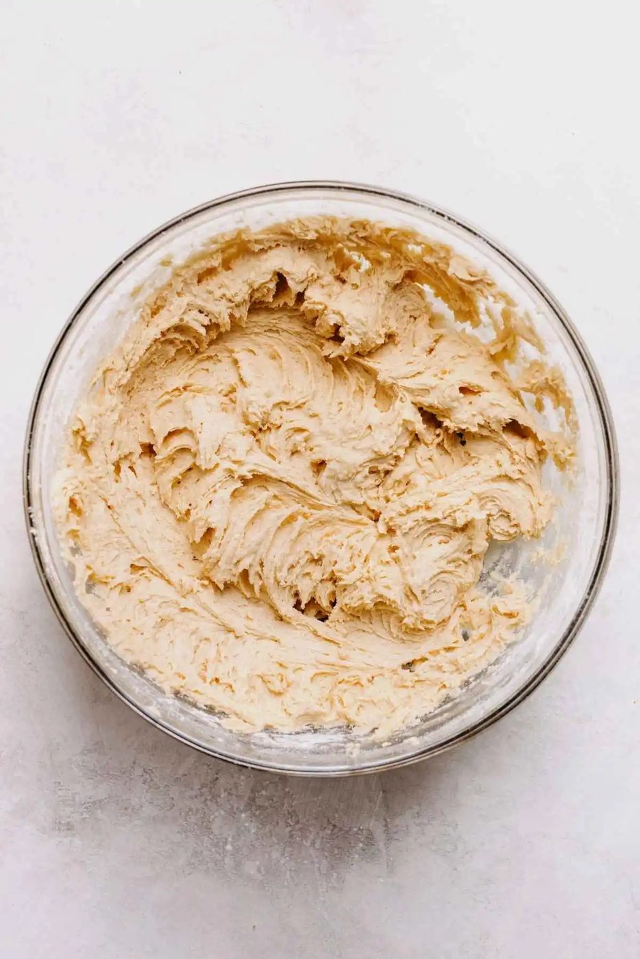 Cookie dough in a large glass mixing bowl on a light grey background.