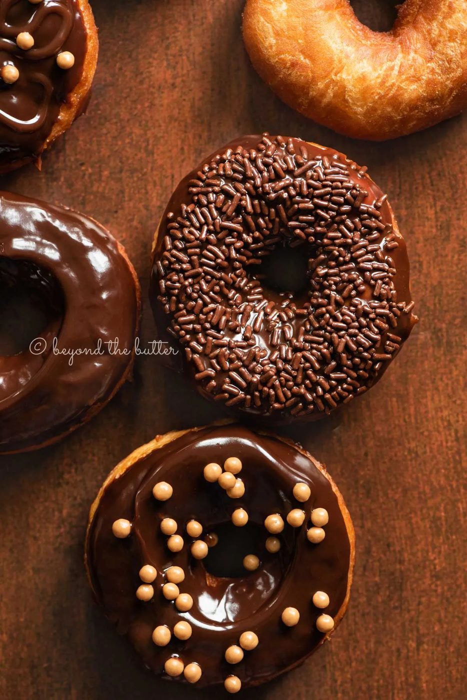 Chocolate glazed decorated donuts on dark wood background | All Images © Sovuh