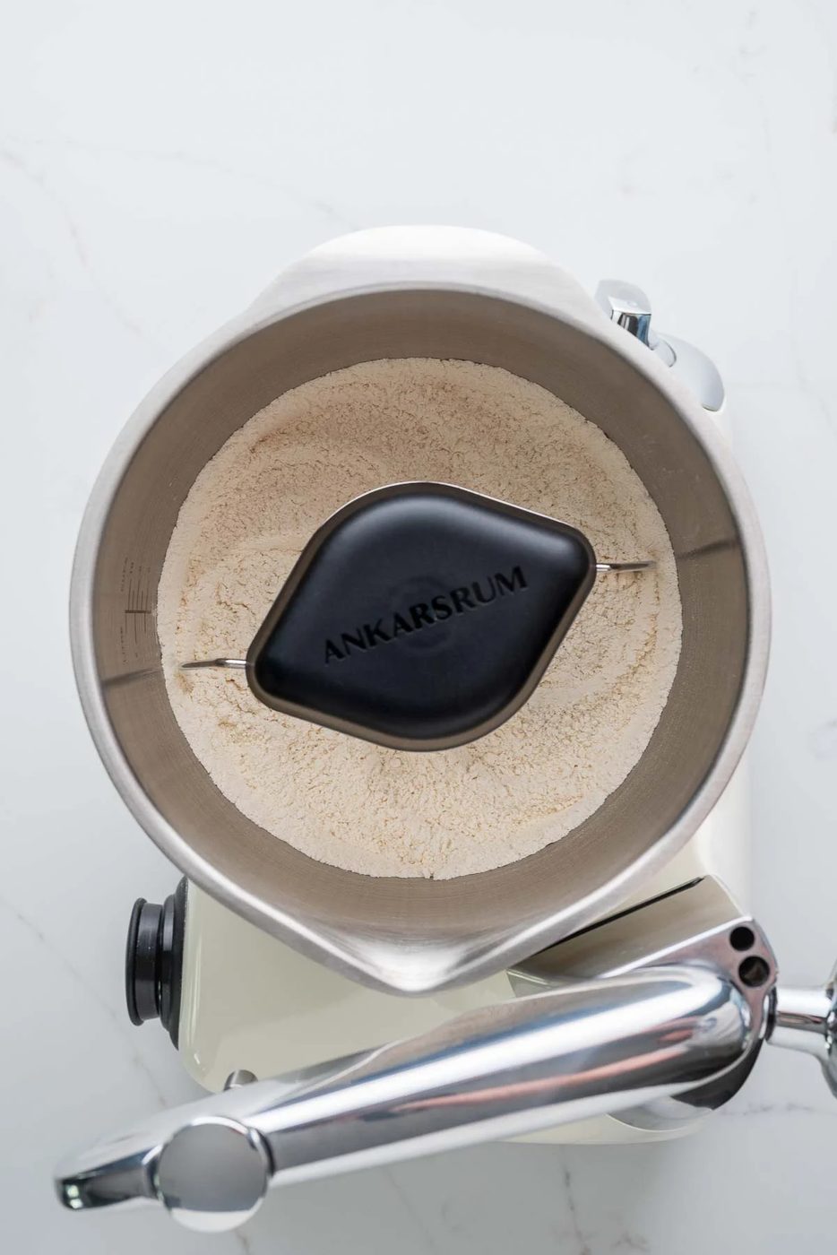 Flour, salt, and sugar mixed together in a creme light colored ankarsrum assistent original mixer and stainless steel beater bowl with their new premium beater set.