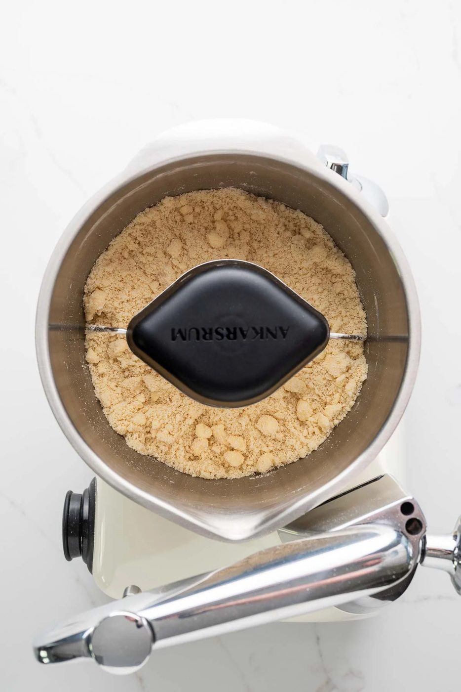 Flour, salt, sugar, and cold cubed butter mixed together in a creme light colored ankarsrum assistent original mixer and stainless steel beater bowl with their new premium beater set.