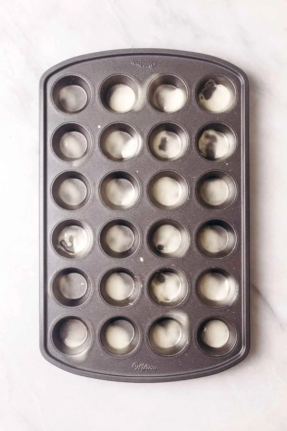 Non stick coated twenty four cavity mini muffin pan sprayed with baking spray on white textured background.