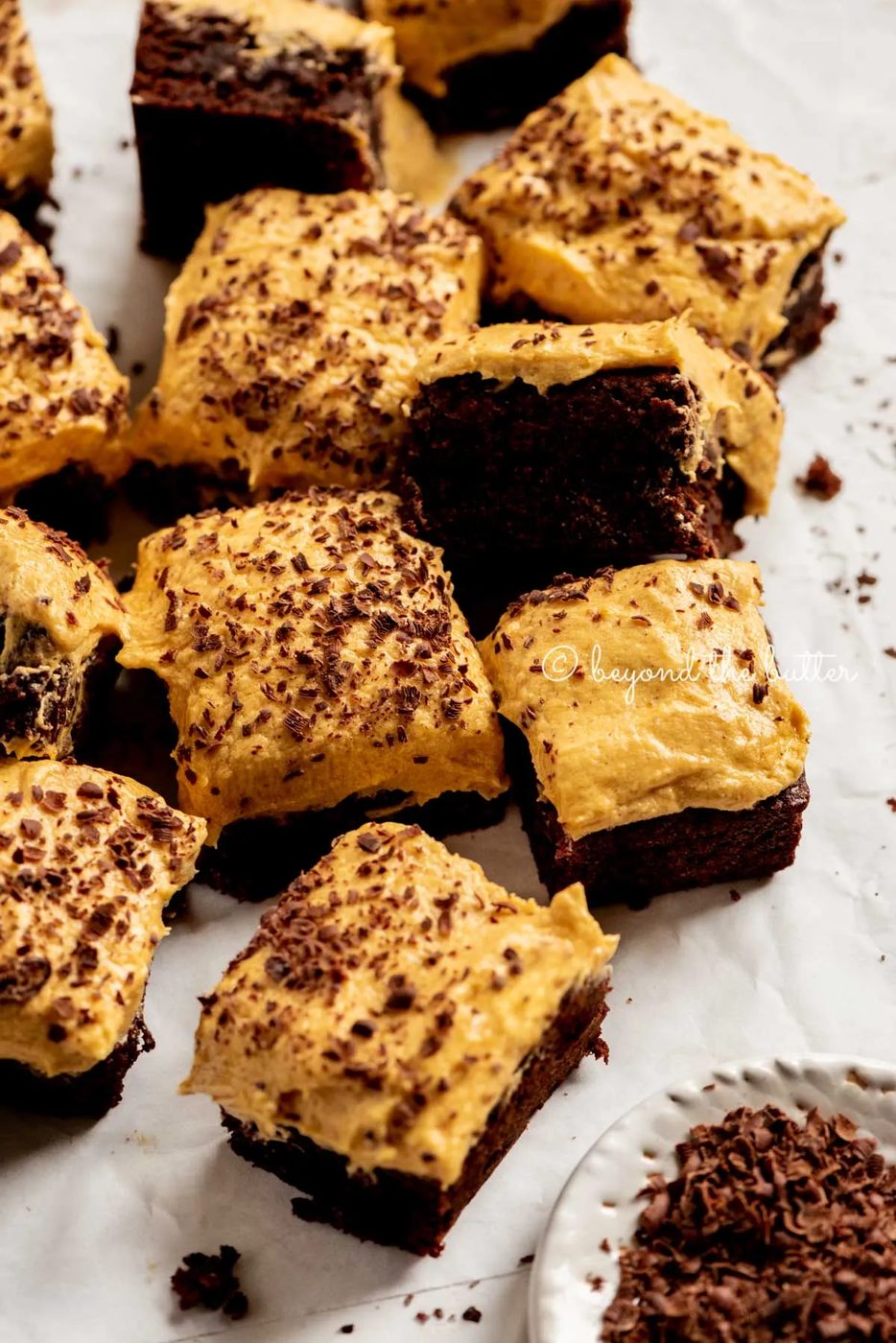pumpkin frosted brownies randomly placed on parchment paper with a side bowl of chocolate shavings | All Images © Sovuh