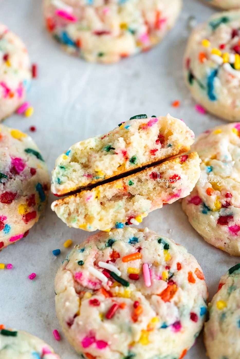 Funfetti butter cookies on a parchment paper lined baking sheet with the center cookie split in half.