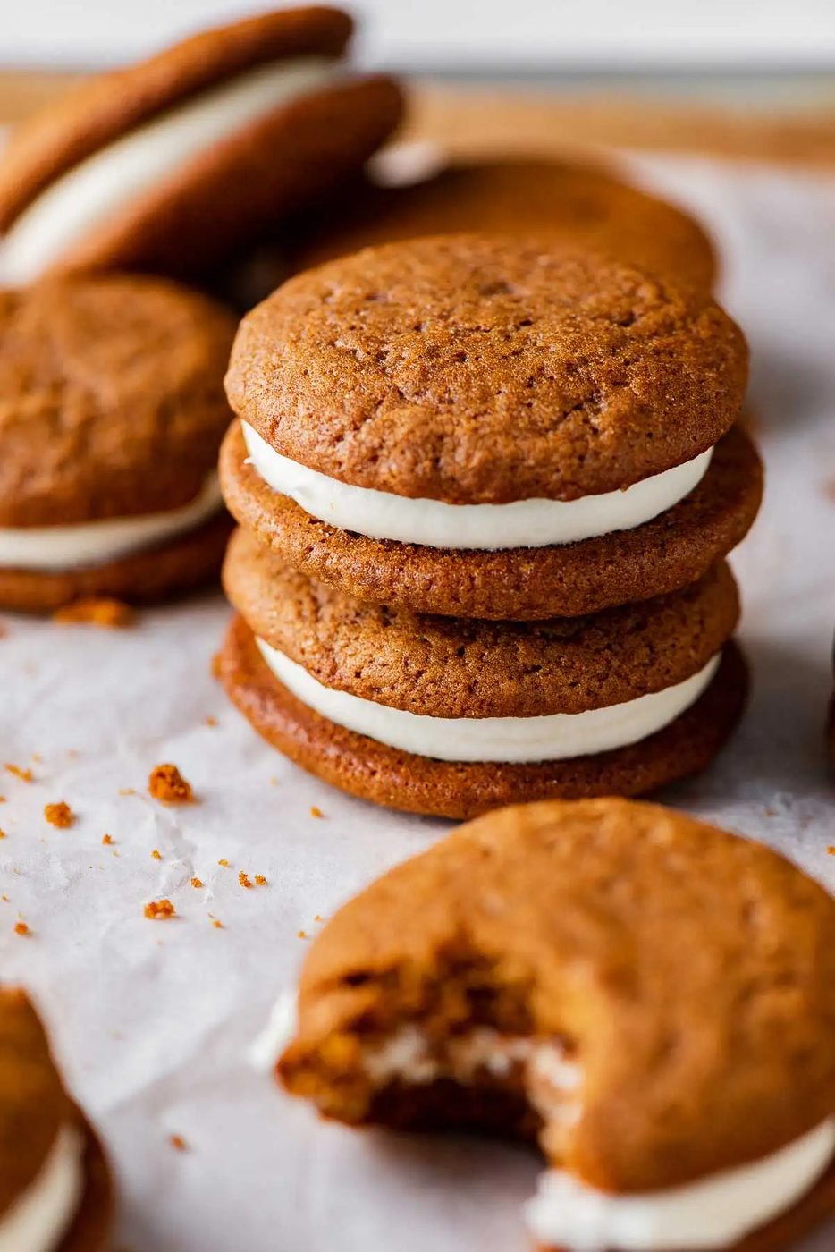 Stacked gingerbread whoopie pies filled with cream cheese frosting on a parchment paper lined baking sheet | © Sovuh