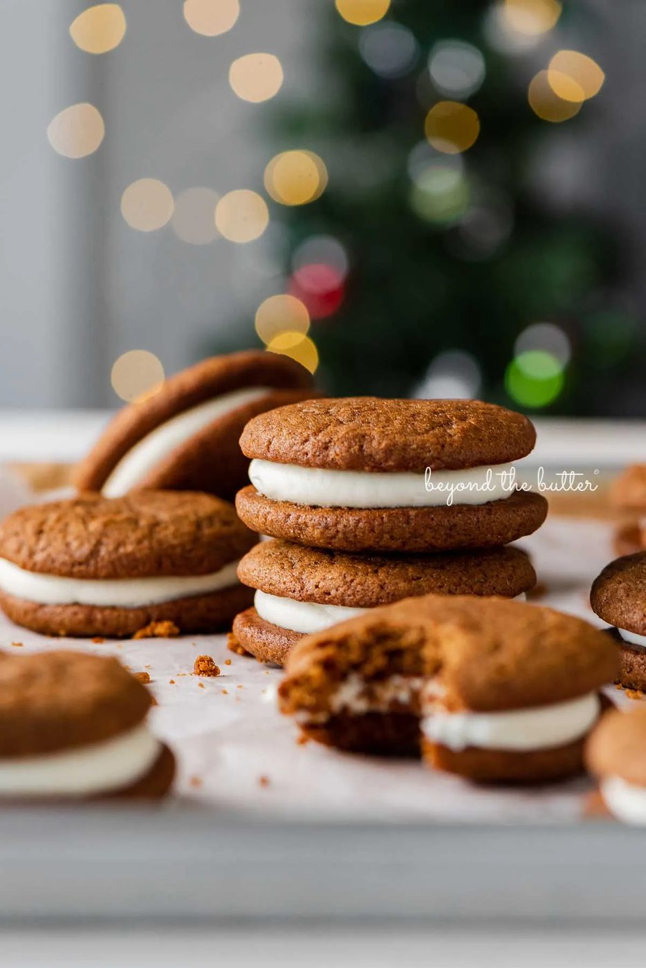 Stacked gingerbread whoopie pies on white parchment paper with holiday tree background | © Sovuh