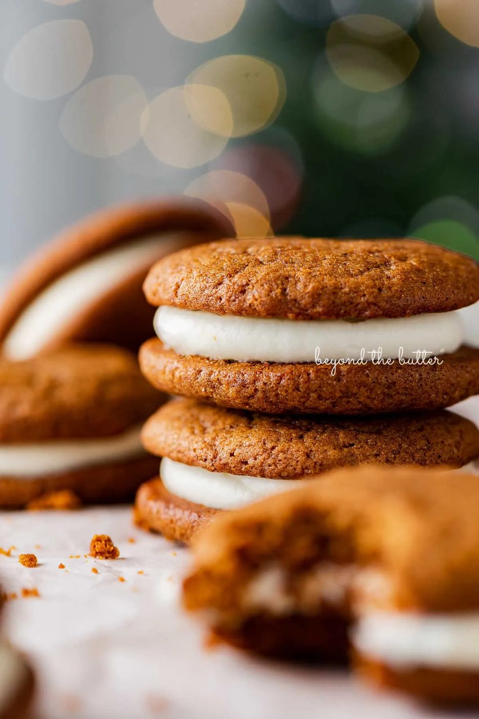 Stacked gingerbread whoopie pies on white parchment paper with holiday tree background | © Sovuh