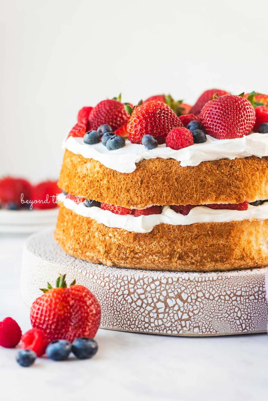 House-made angel food cake layered with cool whip and fresh berries on a ceramic cake stand with a white background | © Sovuh