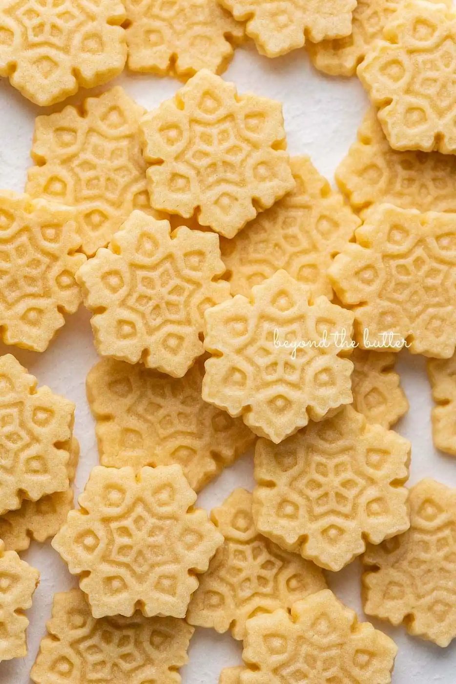 Butter cookies shaped as snowflakes randomly placed on a white parchment paper lined baking sheet.