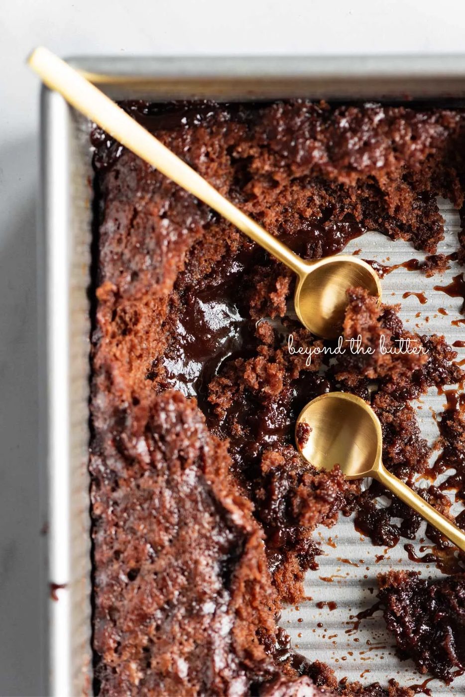 Small gold spoons resting in a baking tin of hot fudge pudding cake.