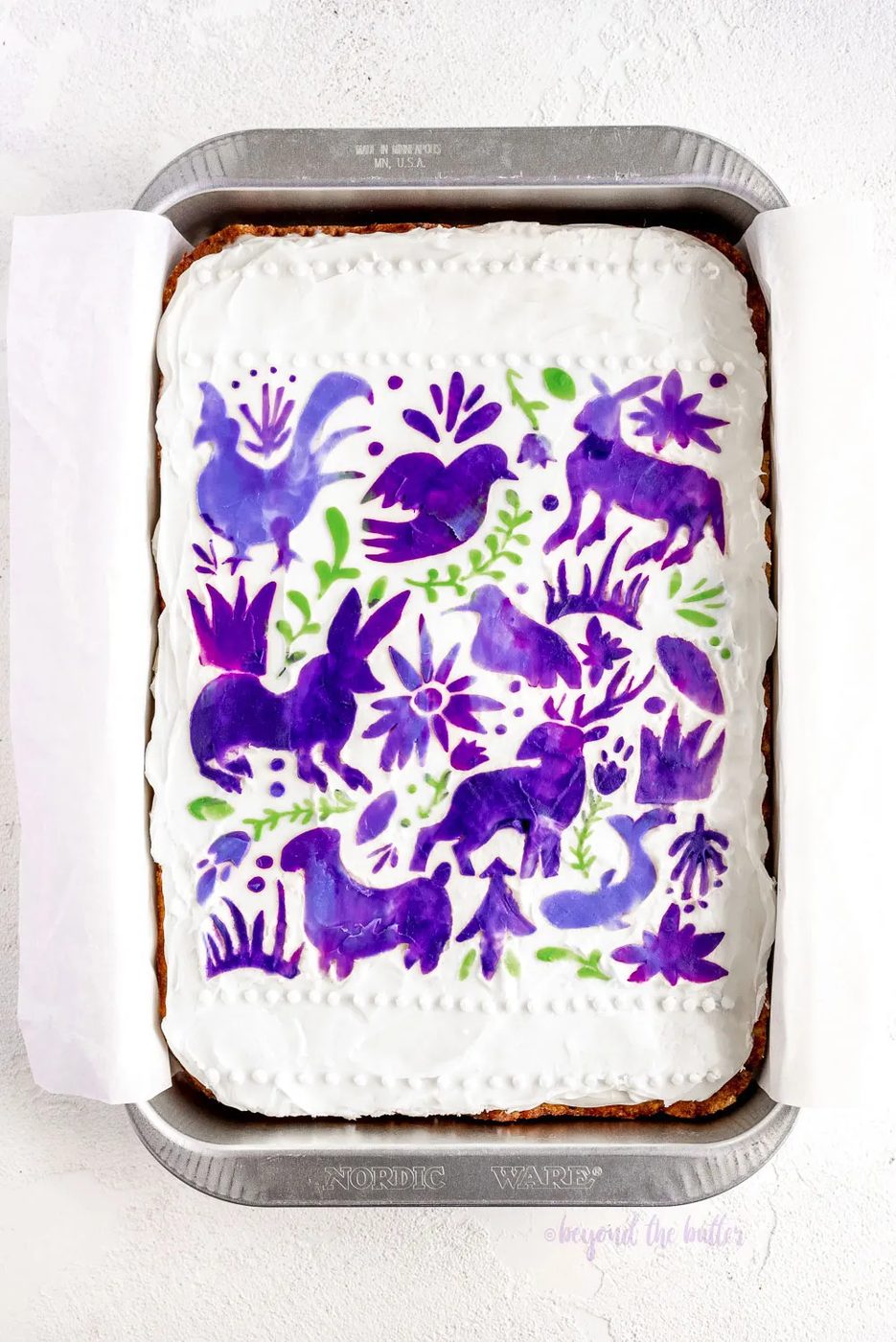 Hummingbird Sheet Cake with White Chocolate Cream Cheese Frosting | Overhead photo of Hummingbird Sheet Cake that's topped with a white chocolate frosting, and stenciled using purple and green frosting | Image and Copyright Policy: © Sovuh, LLC.