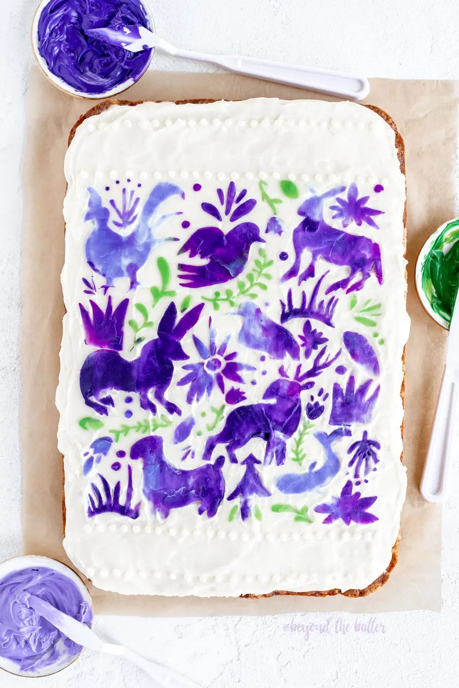 Hummingbird Sheet Cake with White Chocolate Cream Cheese Frosting | Overhead photo of Hummingbird Sheet Cake that's topped with a white chocolate frosting, and stenciled using purple and green frosting | Image and Copyright Policy: © Sovuh, LLC.