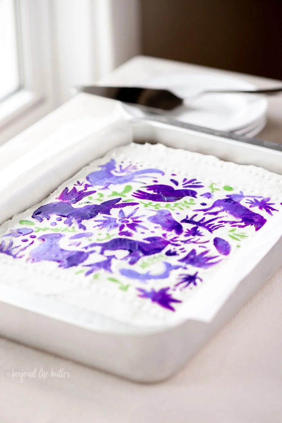 Hummingbird Sheet Cake with White Chocolate Cream Cheese Frosting | Overhead photo of Hummingbird Sheet Cake that's topped with a white chocolate frosting, and stenciled using purple and green frosting | Image and Copyright Policy: © Sovuh, LLC.