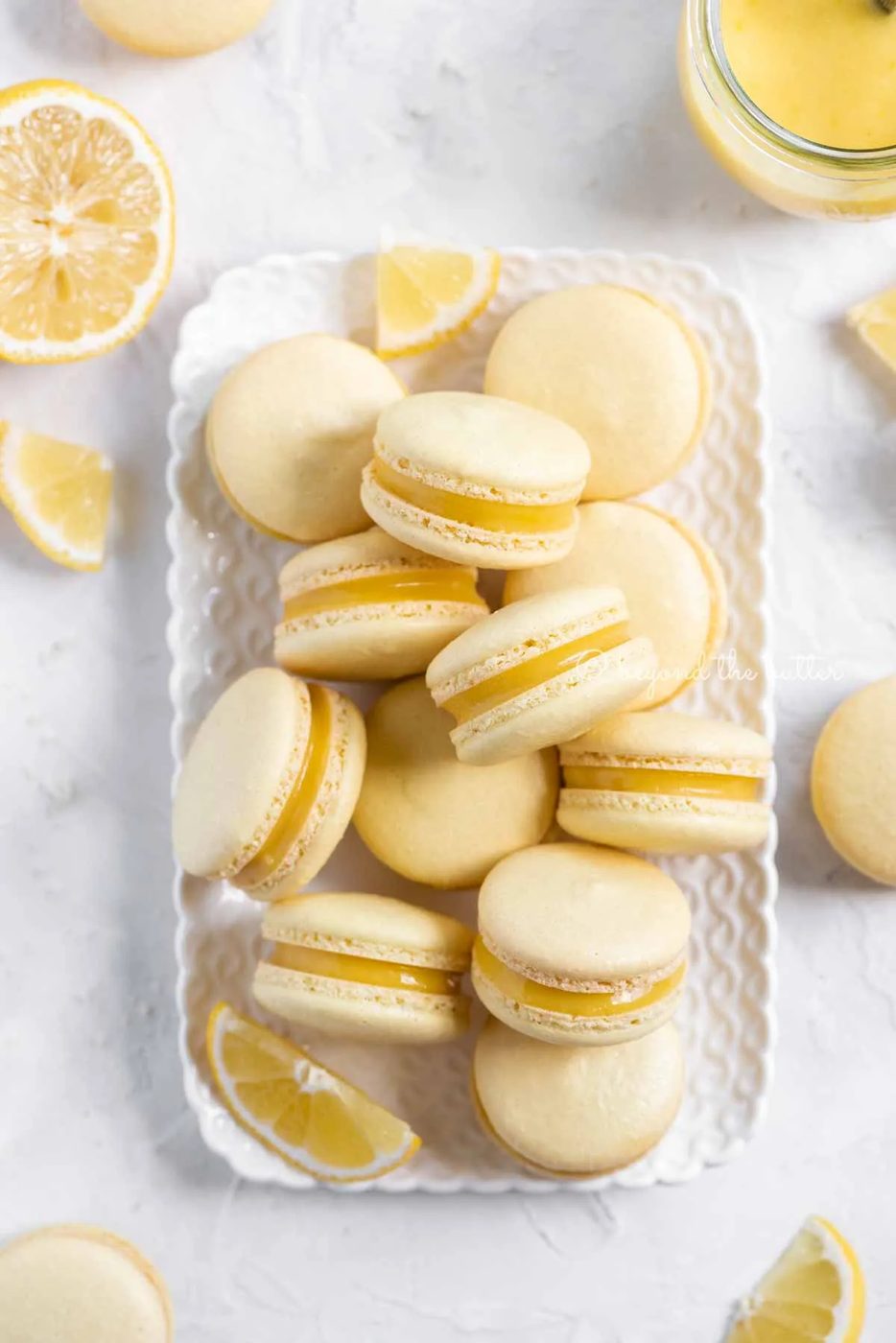Overhead image of lemon bar macarons on a white dessert tray with lemon wedges | All Images © Sovuh