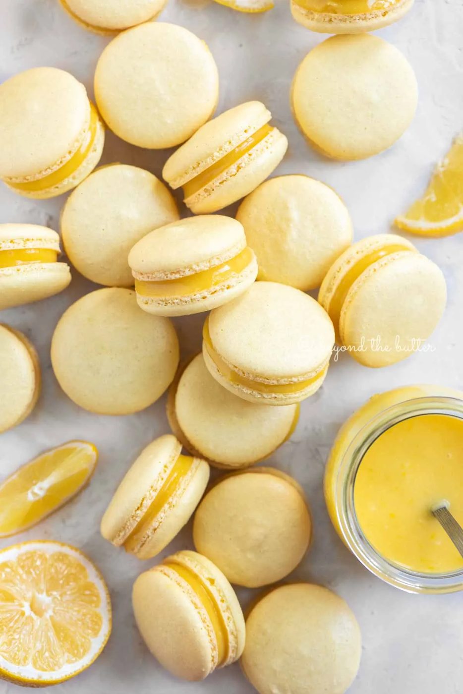 Overhead image of lemon bar macarons randomly placed around a small jar of lemon curd filling | All Images © Sovuh