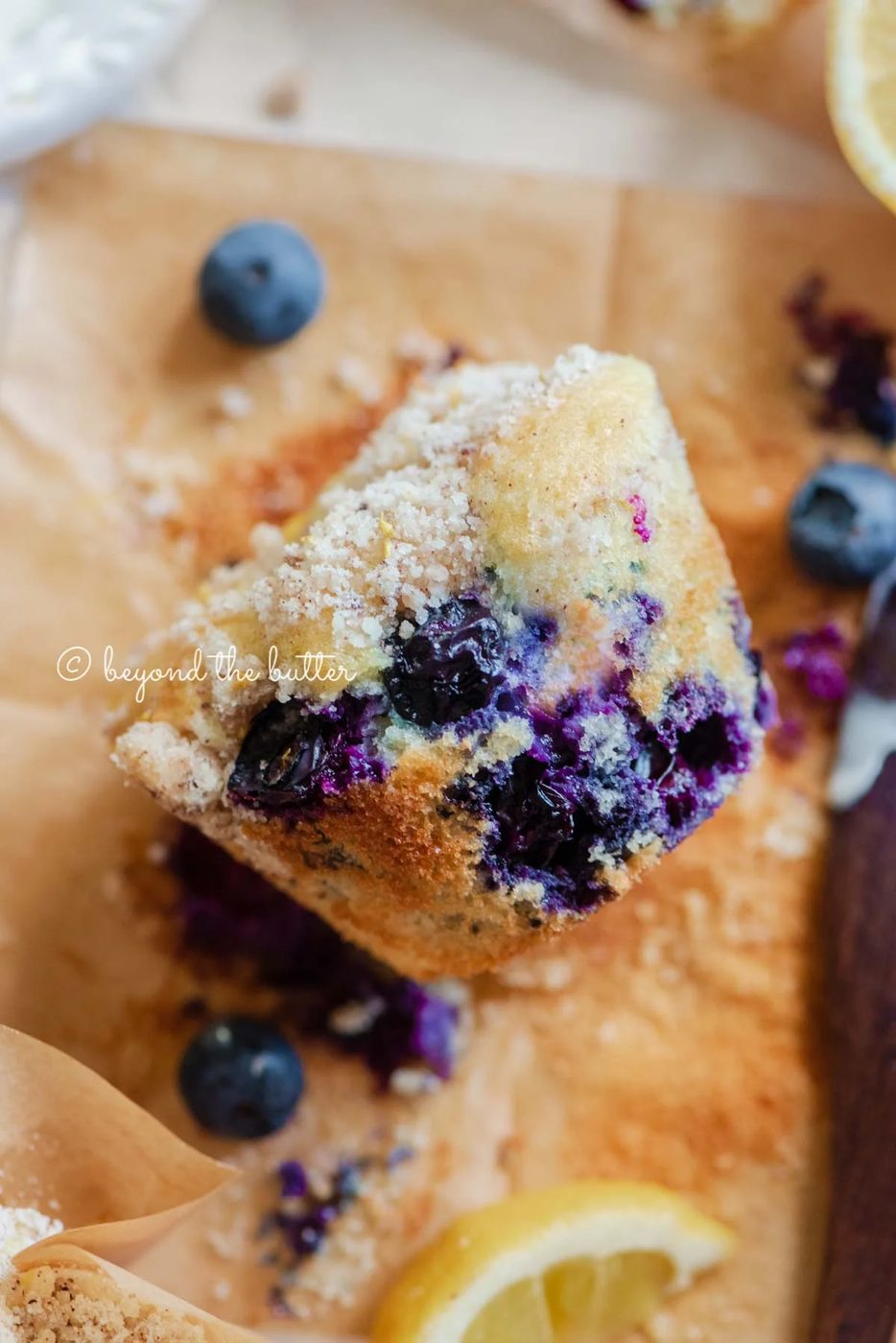 Unwrapped lemon blueberry streusel muffin with lemon wedges and blueberries around it | All images © Sovuh