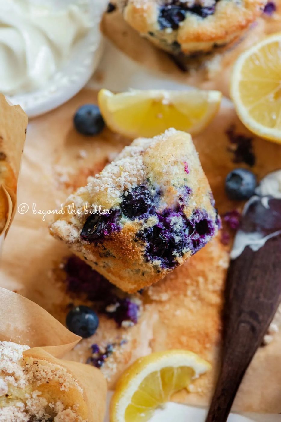 Unwrapped lemon blueberry streusel muffin with small bowl of butter, lemon wedges and blueberries around it | All images © Sovuh