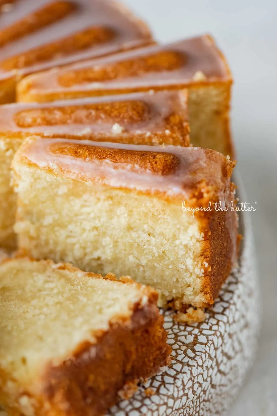 Sliced lemon cream cheese pound cake with a lemon glaze on a cake stand | © Sovuh