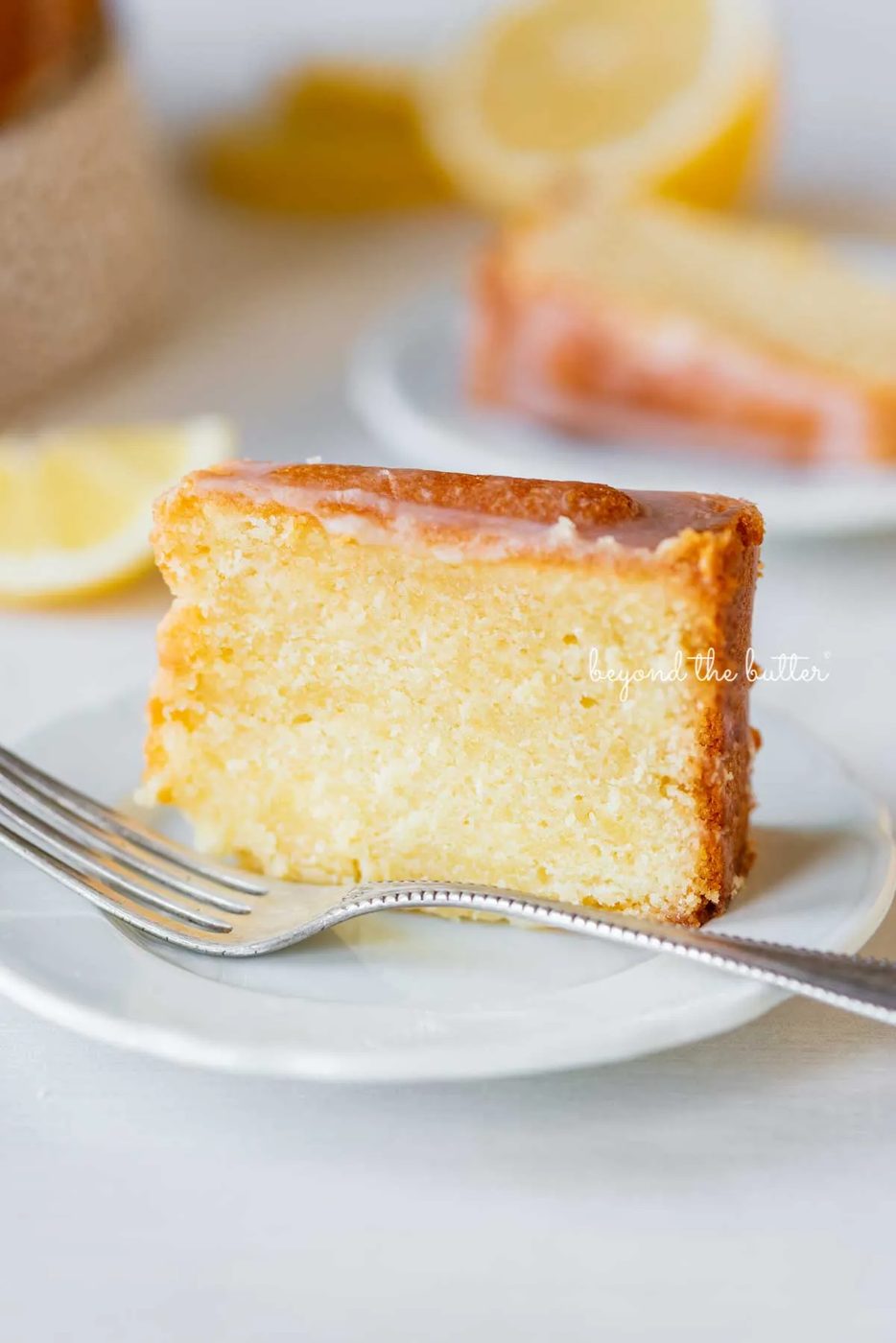 Single slice of glazed lemon cream cheese pound cake on a white dessert plate | © Sovuh